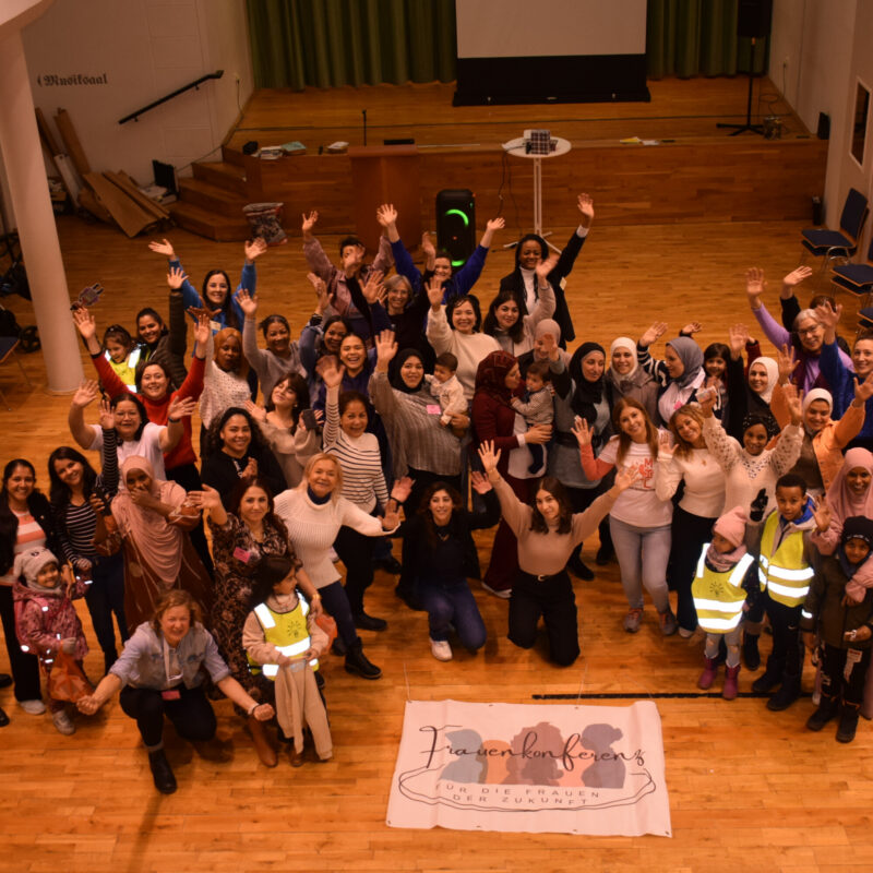 Frauen mit und ohne Migrationsbiografie, mit und ohne Kopftuch, lächeln und winken in die Kamera, welche sie von oben fotografiert