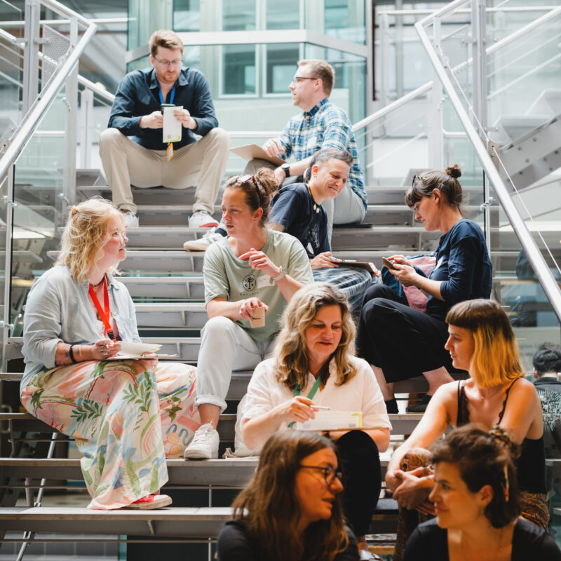 Eine Gruppe Menschen sitzt auf einer Treppe und unterhält sich angeregt.