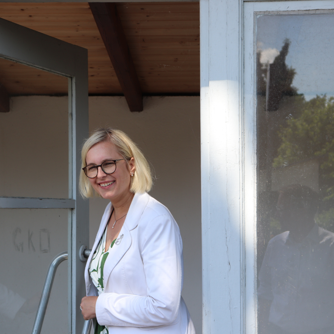 Staatsministerin Frau Christiane Schenderlein lächelt aus einer halbgeöffneten Bushaltestellentür heraus.