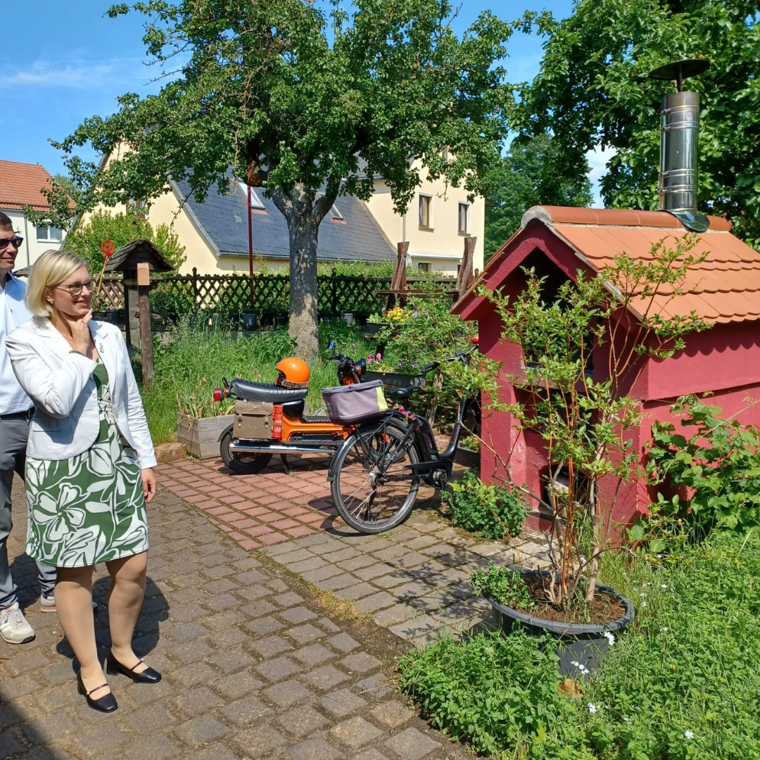 Staatsiminsterin Christiane Schenderlein schaut sich den Außenbereich der Umweltstation Nauendorf, hier genauer eine kleine rote Hütte mi Kaminrohr an.