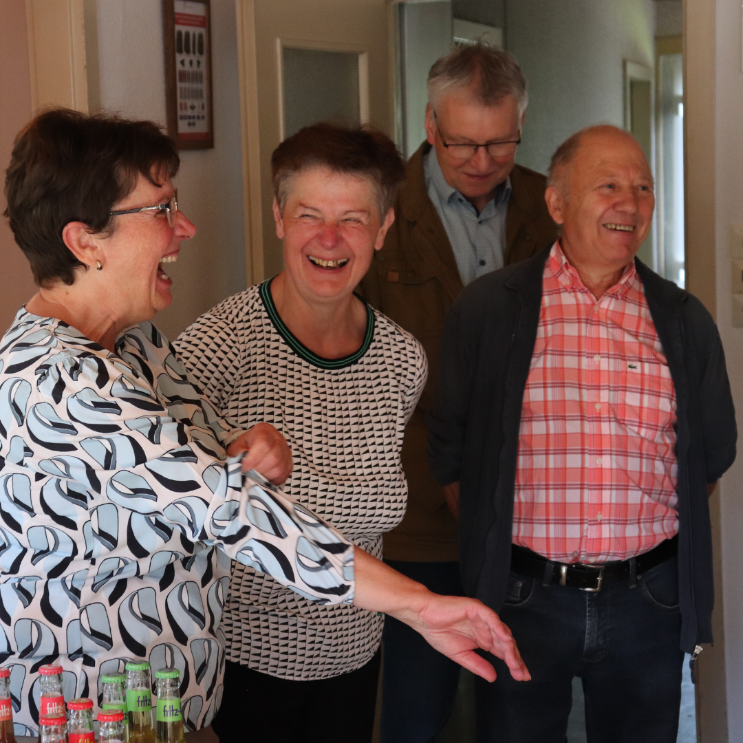 Vier Ältere Menschen lachen herzlich. Die Frau ganz vorne. zeiht sich den Ärmel hoch.