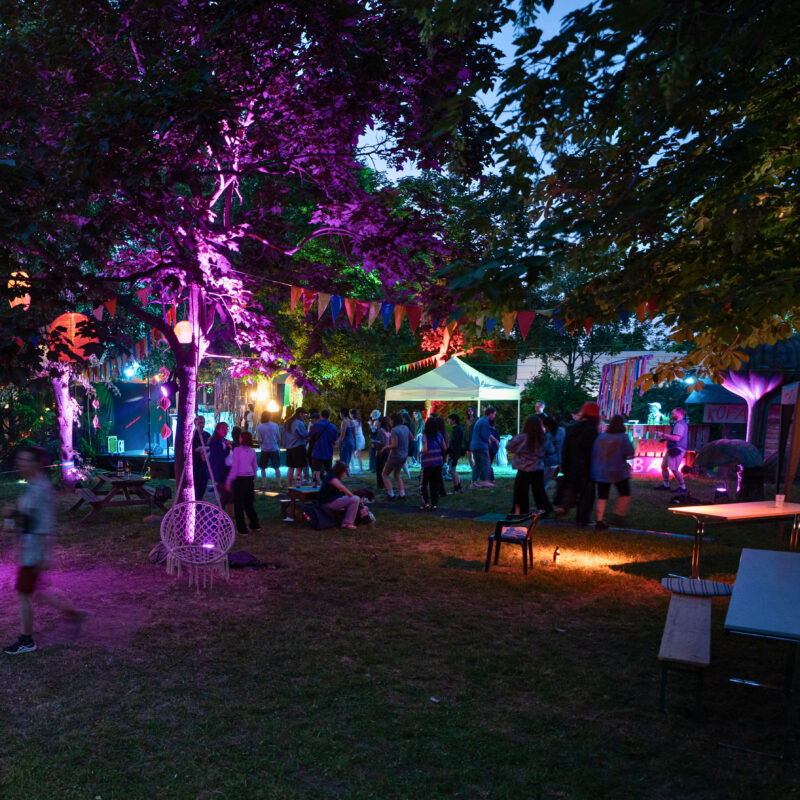 In einem nächtlichen Garten leuchten bunte Lichter und Menschen sind unterwegs